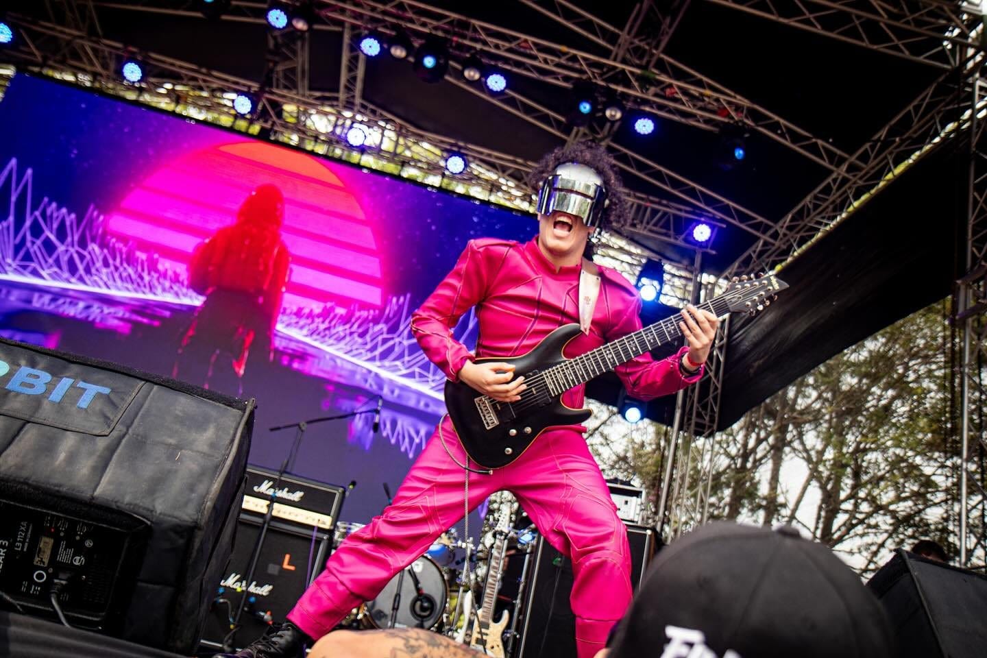 El guitarrista de Rex Marte, de rosado, frente a una pantalla de neón