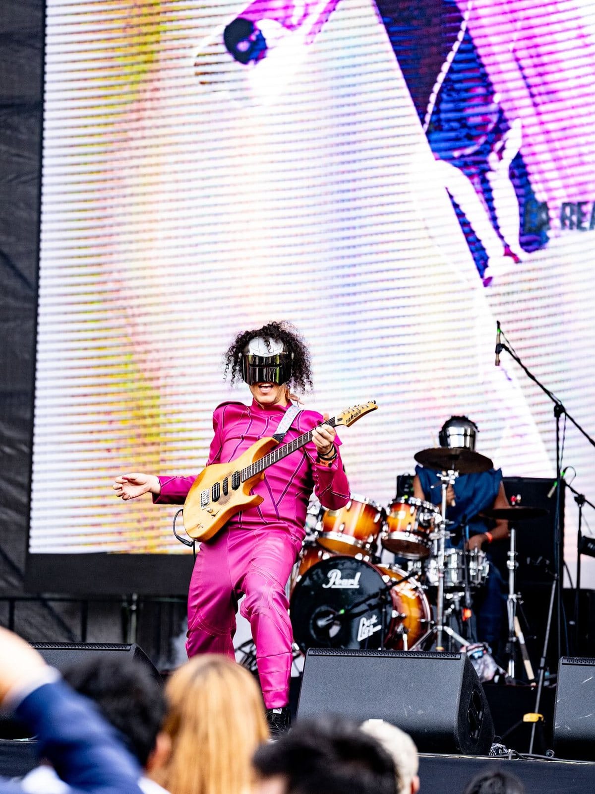 El guitarrista de Rex Marte, de rosado, frente a la pantalla del escenario